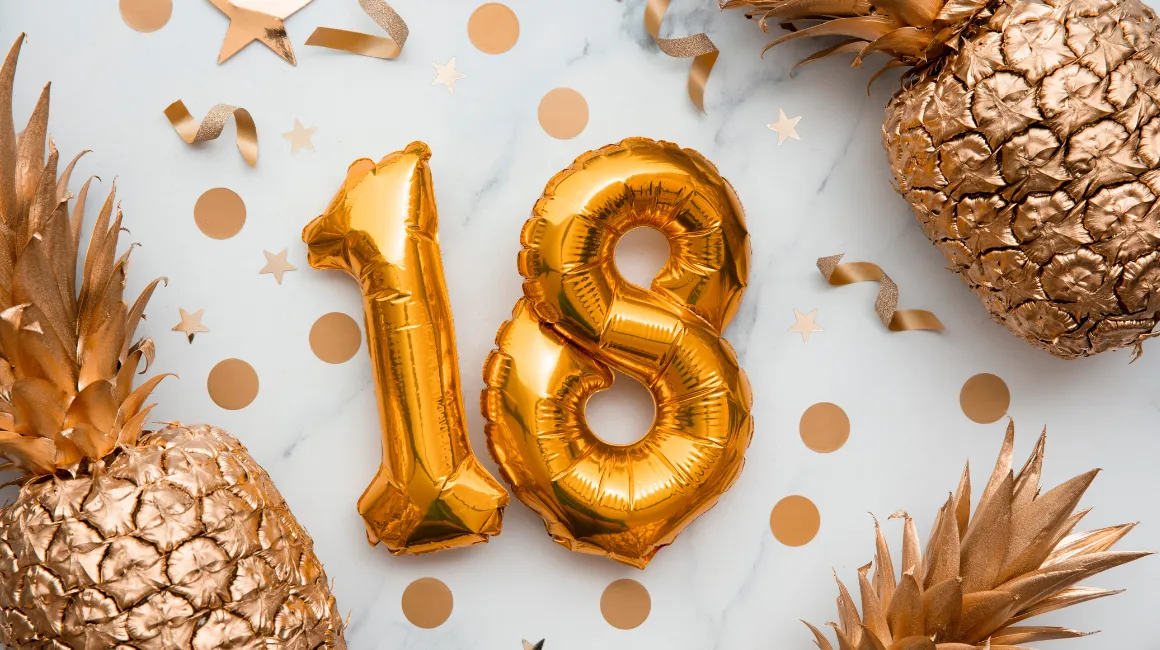 Dekoracja urodzinowa z balonami w kształcie liczby 18, złotymi ananasami i konfetti na jasnym tle